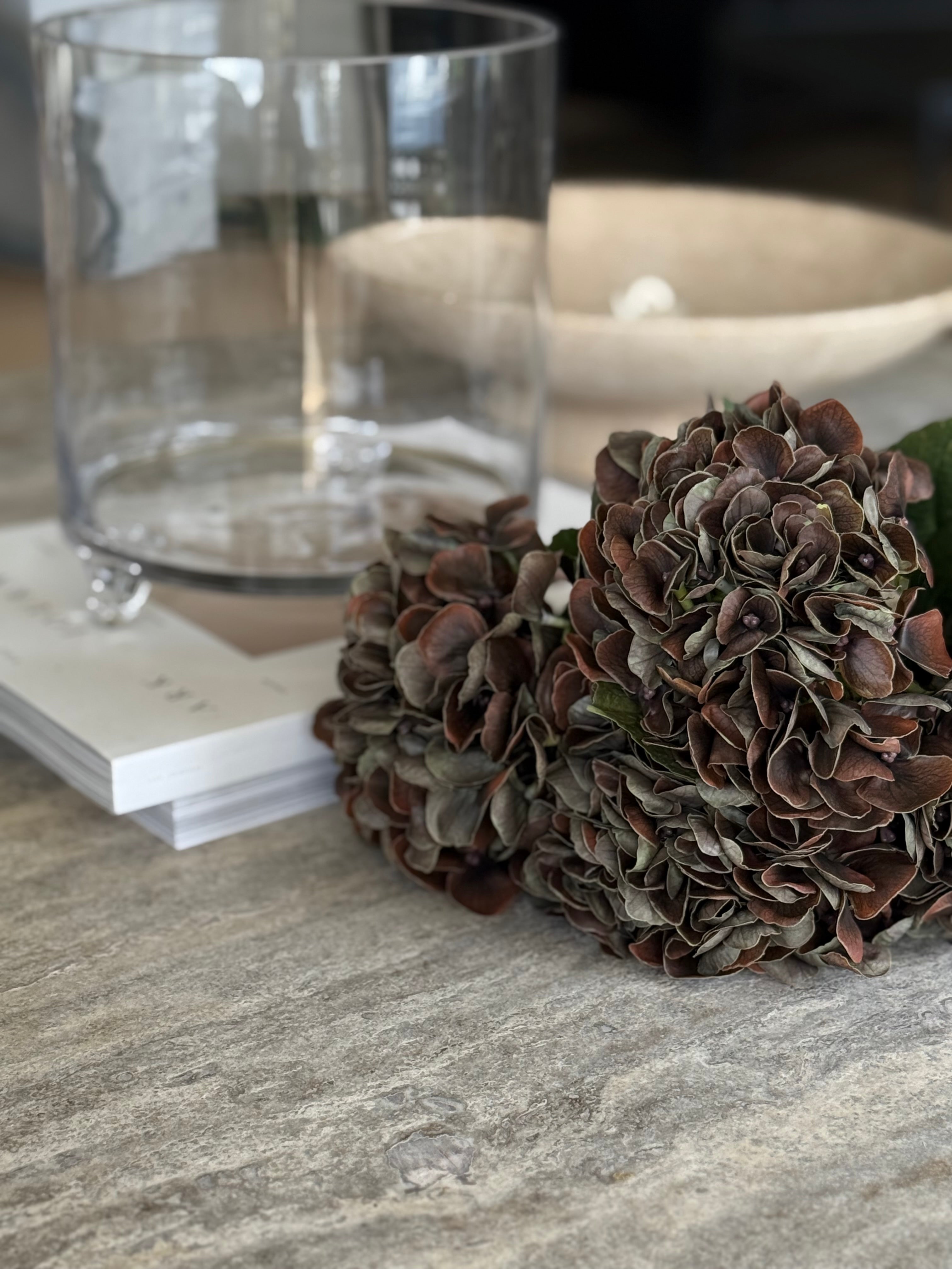 Hortensia mørk brun kunstig, frodig blomsterkule med bøybar stilk mot lys bakgrunn